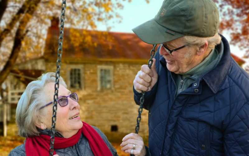 Een oudere vrouw en man bij schommel, de vrouw zit op de schommel